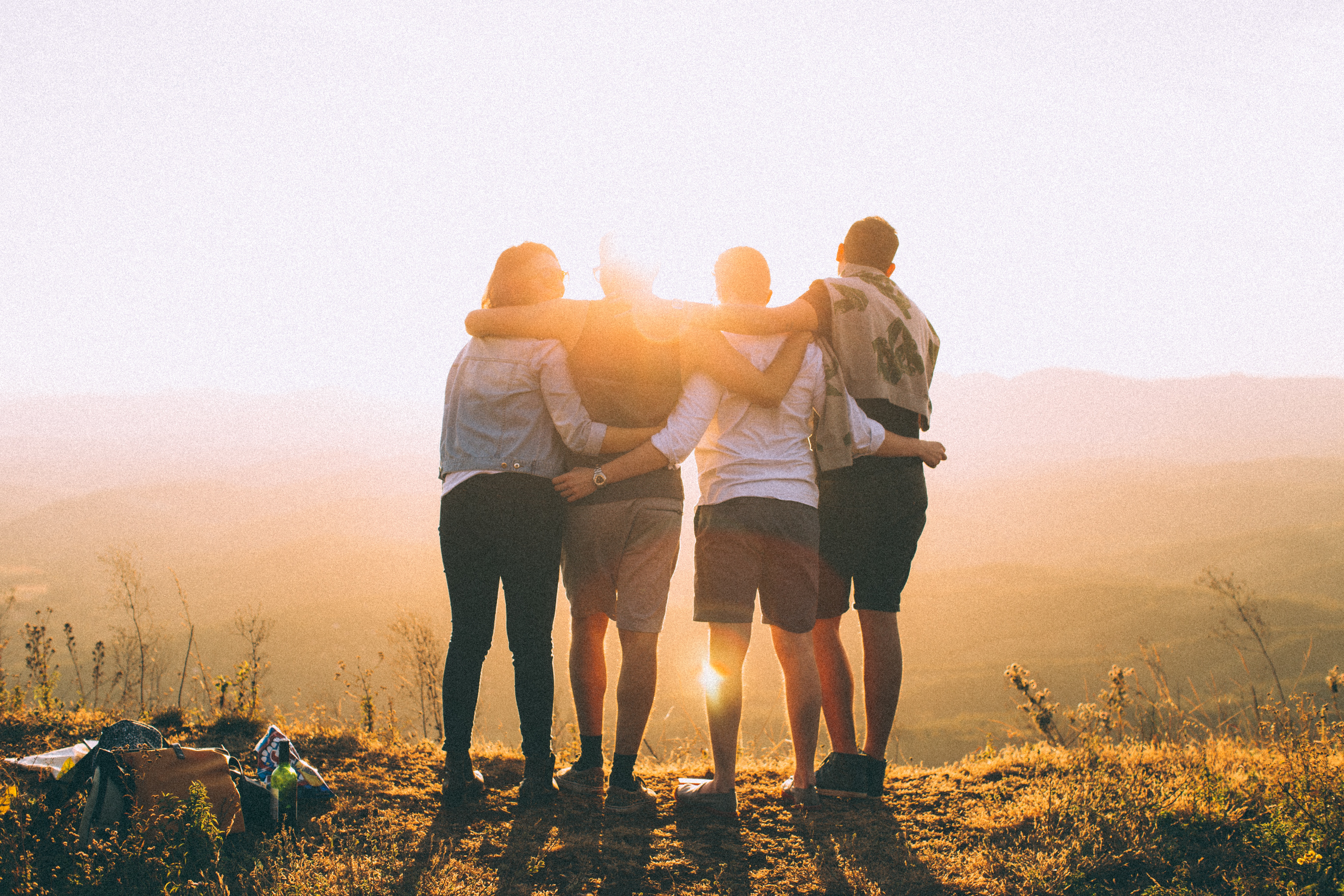Four people with their arms around each other watching a sunset